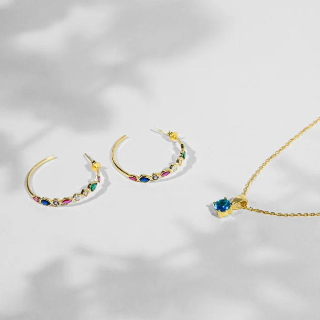 Sidabriniai papuošalai: auskarai, ir pakabukas. Šis spindintis papuošalų rinkinys, pagamintas iš 925 sidabro, sudarytas iš žiedinių auskarų poros ir patrauklaus kaklo pakabuko, yra gyvybingos elegancijos įkūnijimas. Auskarai papuošti įvairiaspalviais kubiniais cirkonijais, sukuria žaismingą, tačiau rafinuotą šviesos spektrą.