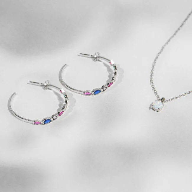 Sidabriniai papuošalai: auskarai, ir pakabukas. Šis spindintis papuošalų rinkinys, pagamintas iš 925 sidabro, sudarytas iš žiedinių auskarų poros ir patrauklaus kaklo pakabuko, yra gyvybingos elegancijos įkūnijimas. Auskarai papuošti įvairiaspalviais kubiniais cirkonijais, sukuria žaismingą, tačiau rafinuotą šviesos spektrą.