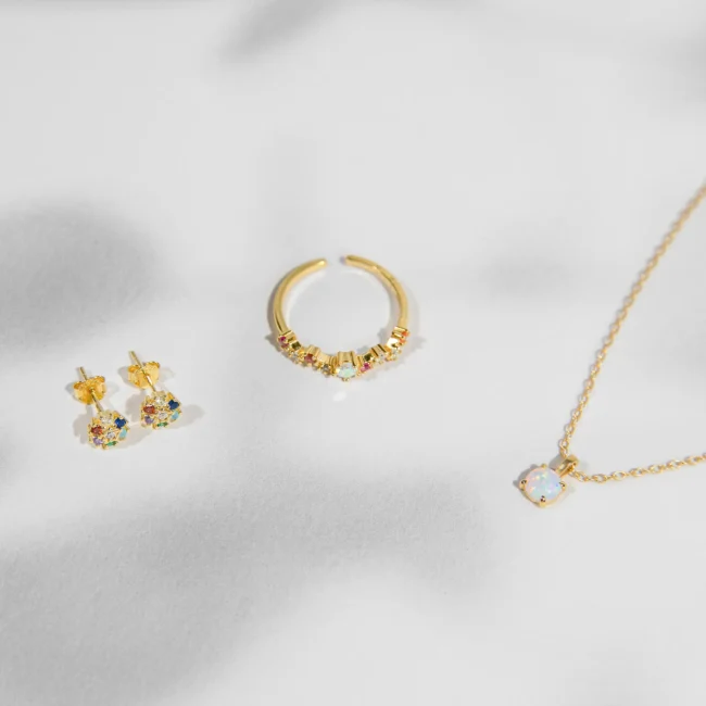 Sidabriniai papuošalai: auskarai, žiedas ir pakabukas. Šis elegantiškas 923 prabos sidabro papuošalų rinkinys, įkūnija šiltą eleganciją ir subtilų prabangos pojūtį. Komplektą sudaro pora žavios formos auskarų, puoštų spalvotais kubiniais cirkoniais, kurie suteikia žaismingą ir gyvybingą išvaizdą, žiedo ir minimalistinio dizaino kaklo papuošalo su kubiniu cirkoniu, kuris sukuria subtilų žavesio akcentą. Papuošalai dengti auksu, atspindi šilumą ir šviesą, papildydami bet kokią aprangą elegancija bei spindesiu.